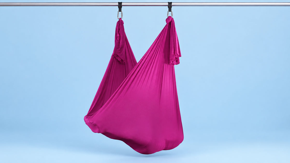 Pinkes Aerial Yoga Tuch an zwei Punkten als Hängematte aufgehängt vor blauem Hintergrund