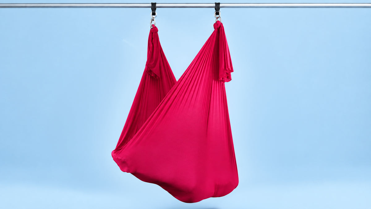 Rotes Aerial Yoga Tuch an zwei Punkten als Hängematte aufgehängt vor blauem Hintergrund
