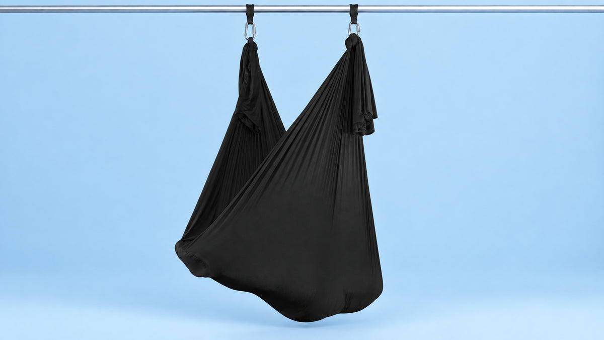 Schwarzes Aerial Yoga Tuch an zwei Punkten als Hängematte aufgehängt vor blauem Hintergrund