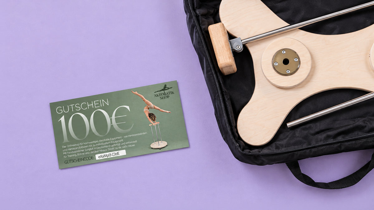 Grüner Geschenkgutschein über 100 Euro neben einer geöffneten schwarzen Tragetasche mit einem Handstandständer aus Holz mit Metallstangen.