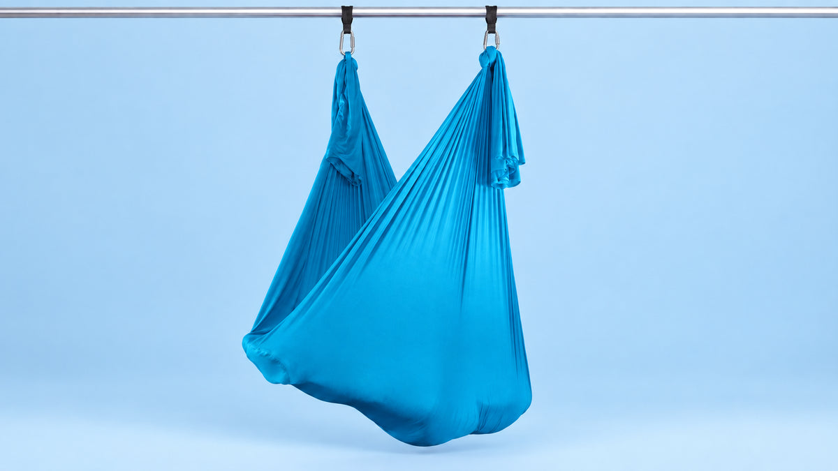 Aquablaues Aerial Yoga Tuch an zwei Punkten als Hängematte aufgehängt vor blauem Hintergrund