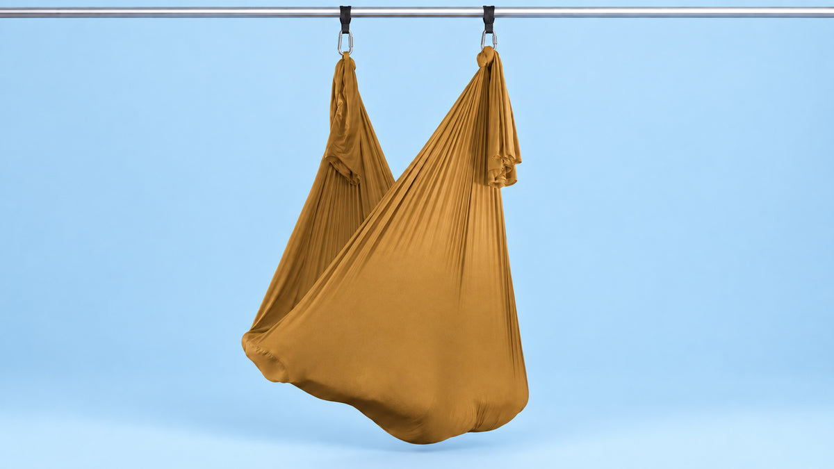 Goldeses Aerial Yoga Tuch an zwei Punkten als Hängematte aufgehängt vor blauem Hintergrund