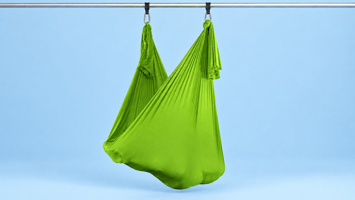 Grünes Aerial Yoga Tuch an zwei Punkten als Hängematte aufgehängt vor blauem Hintergrund