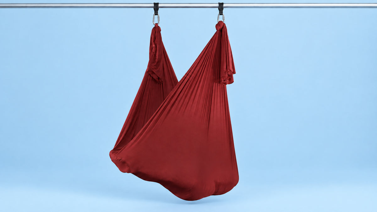 Maroon farbennes Aerial Yoga Tuch an zwei Punkten als Hängematte aufgehängt vor blauem Hintergrund