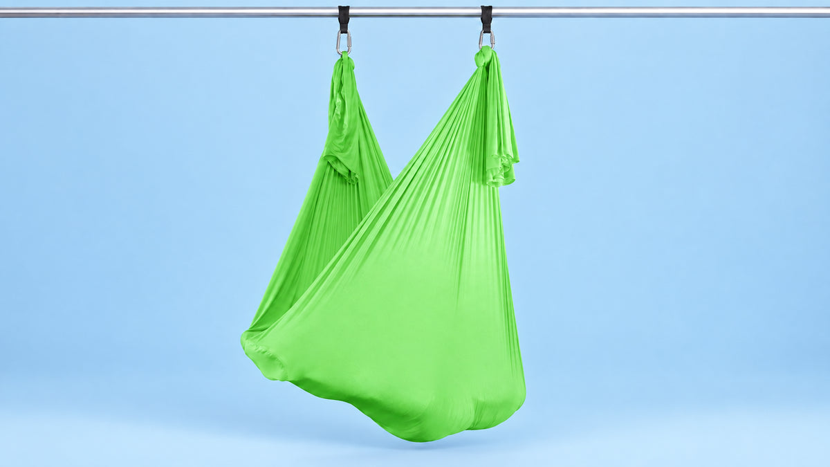 Neon-grünes Aerial Yoga Tuch an zwei Punkten als Hängematte aufgehängt vor blauem Hintergrund