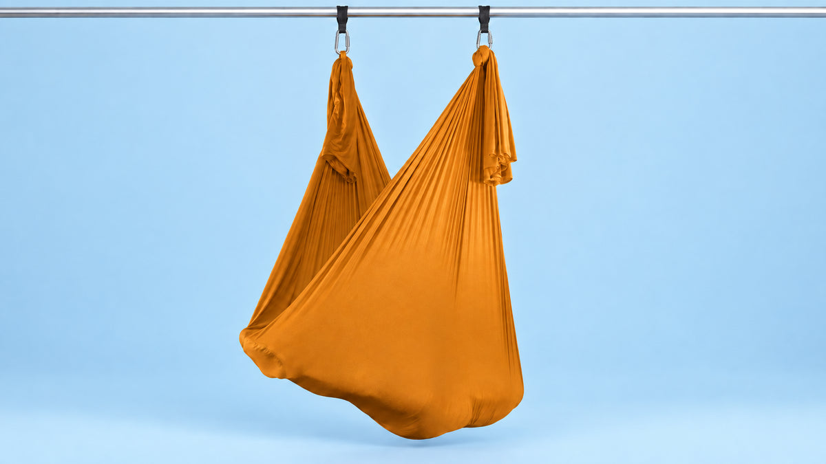 Orangenes Aerial Yoga Tuch an zwei Punkten als Hängematte aufgehängt vor blauem Hintergrund
