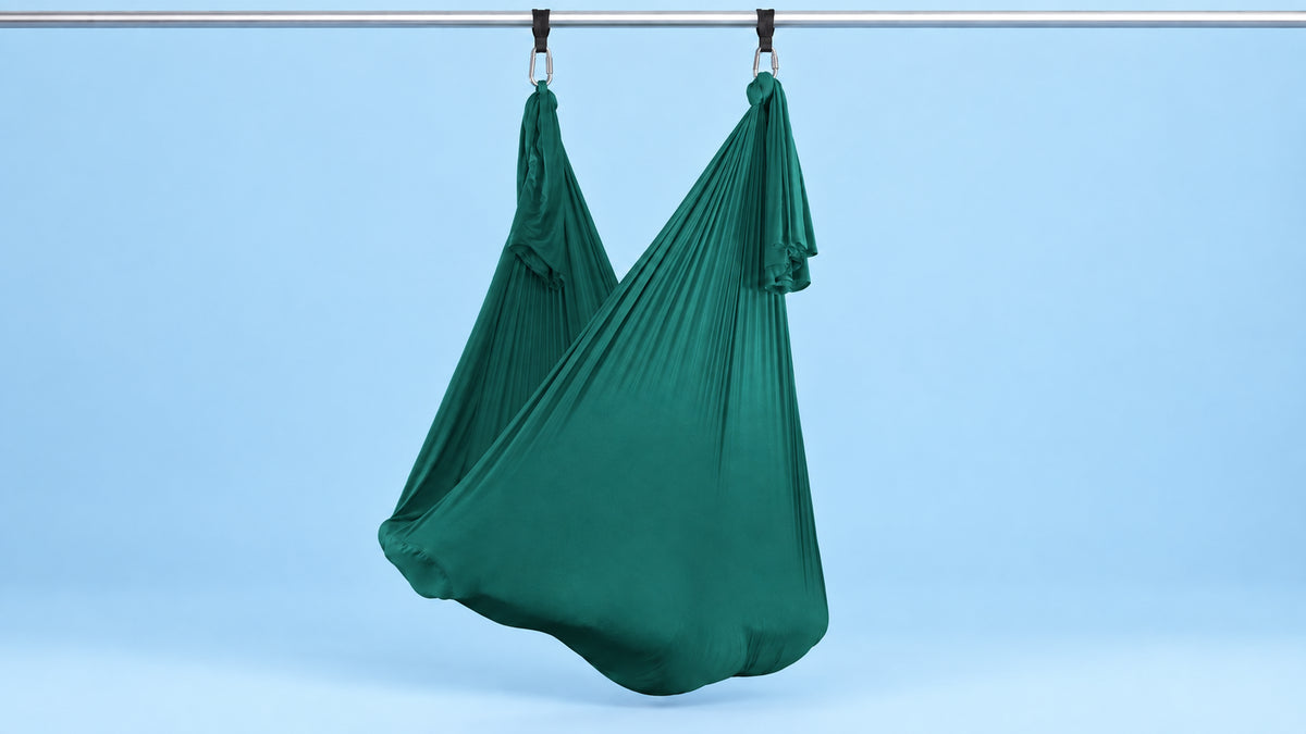 Petrol-grünes Aerial Yoga Tuch an zwei Punkten als Hängematte aufgehängt vor blauem Hintergrund
