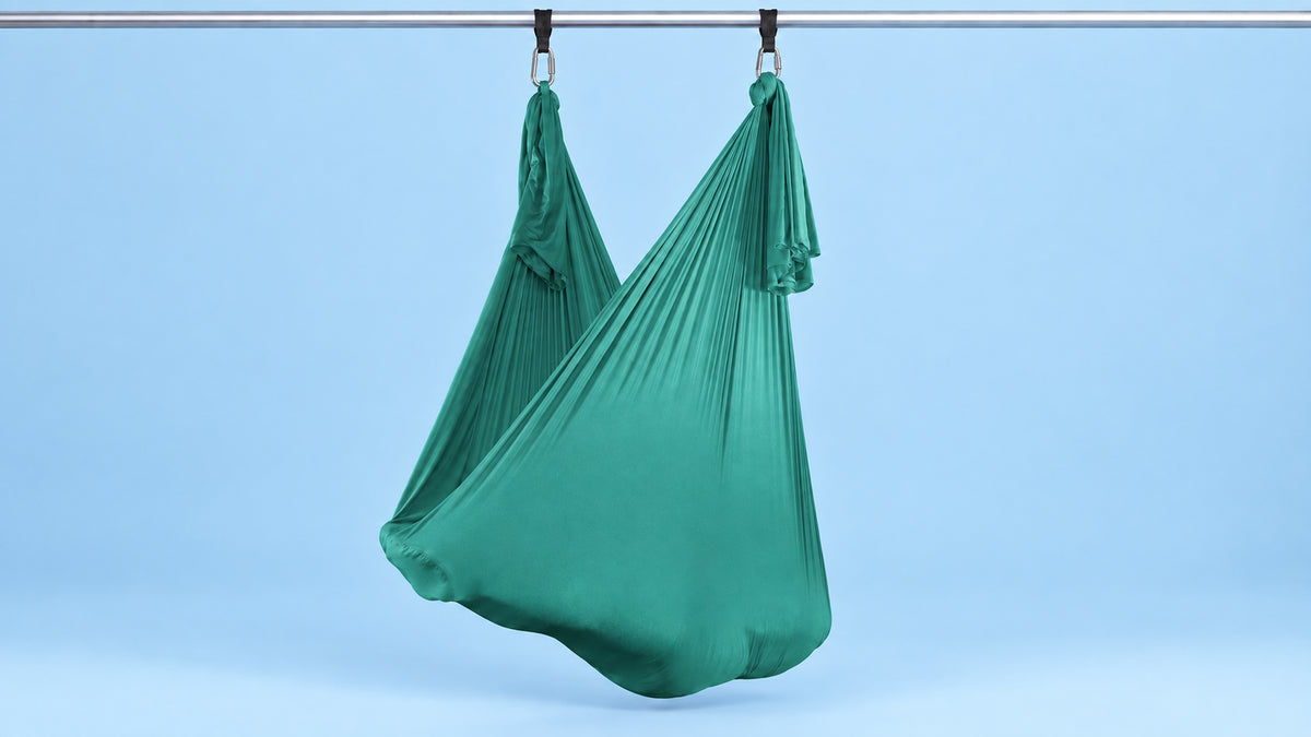 Aerial Yoga Tuch Türkis an zwei Punkten als Hängematte aufgehängt vor blauem Hintergrund