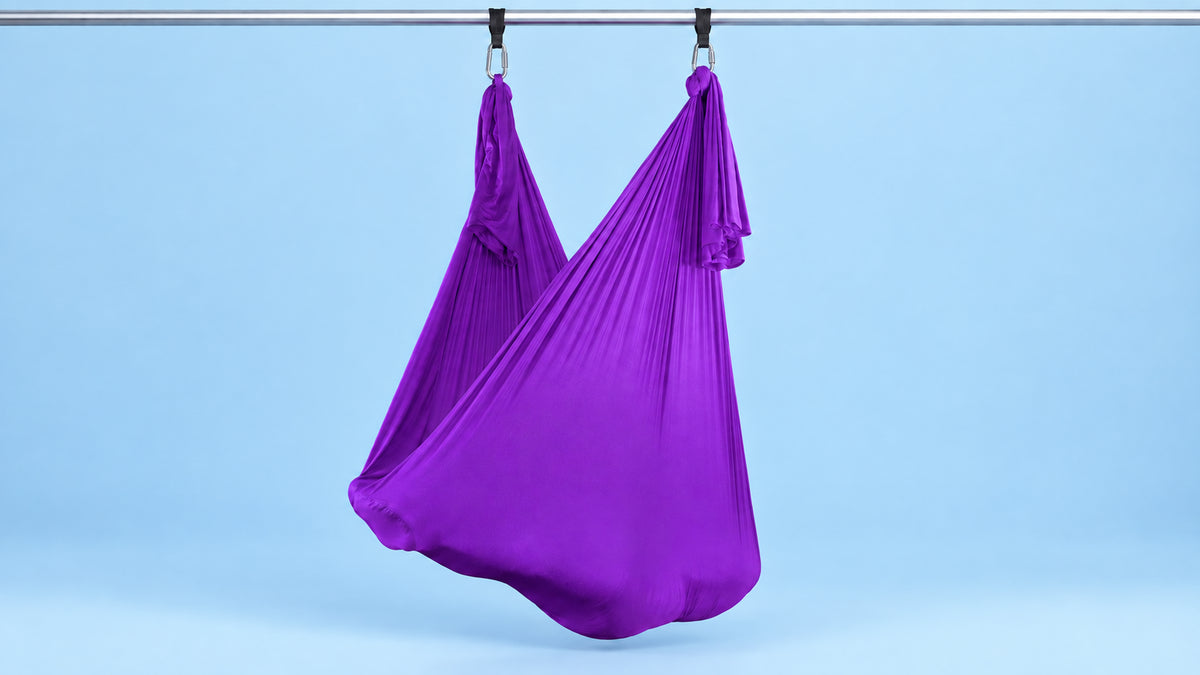 Violetes Aerial Yoga Tuch an zwei Punkten als Hängematte aufgehängt vor blauem Hintergrund
