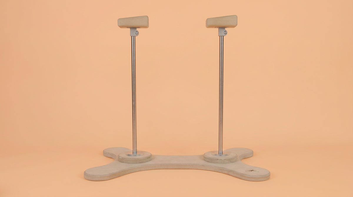 Zwei Handstand Canes mit abgeschrägten Holzgriffen und Metallstangen auf einer knochenförmigen Grundplatte aus Holz vor einfarbigem Hintergrund