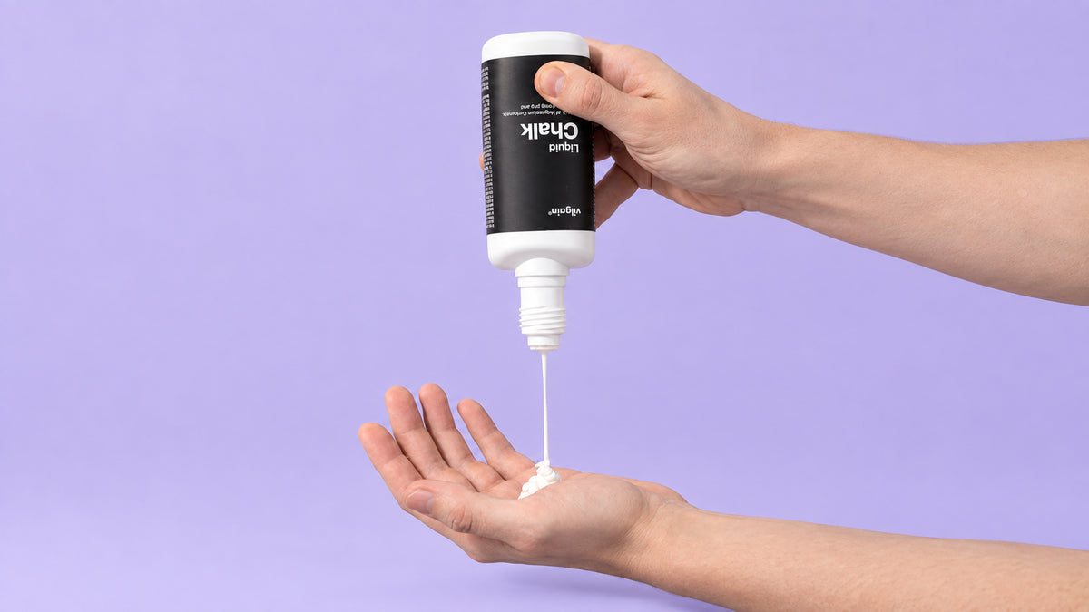 Hand gibt Flüssigkreide aus einer Flasche auf die andere Handfläche vor ein lila Hintergrund
